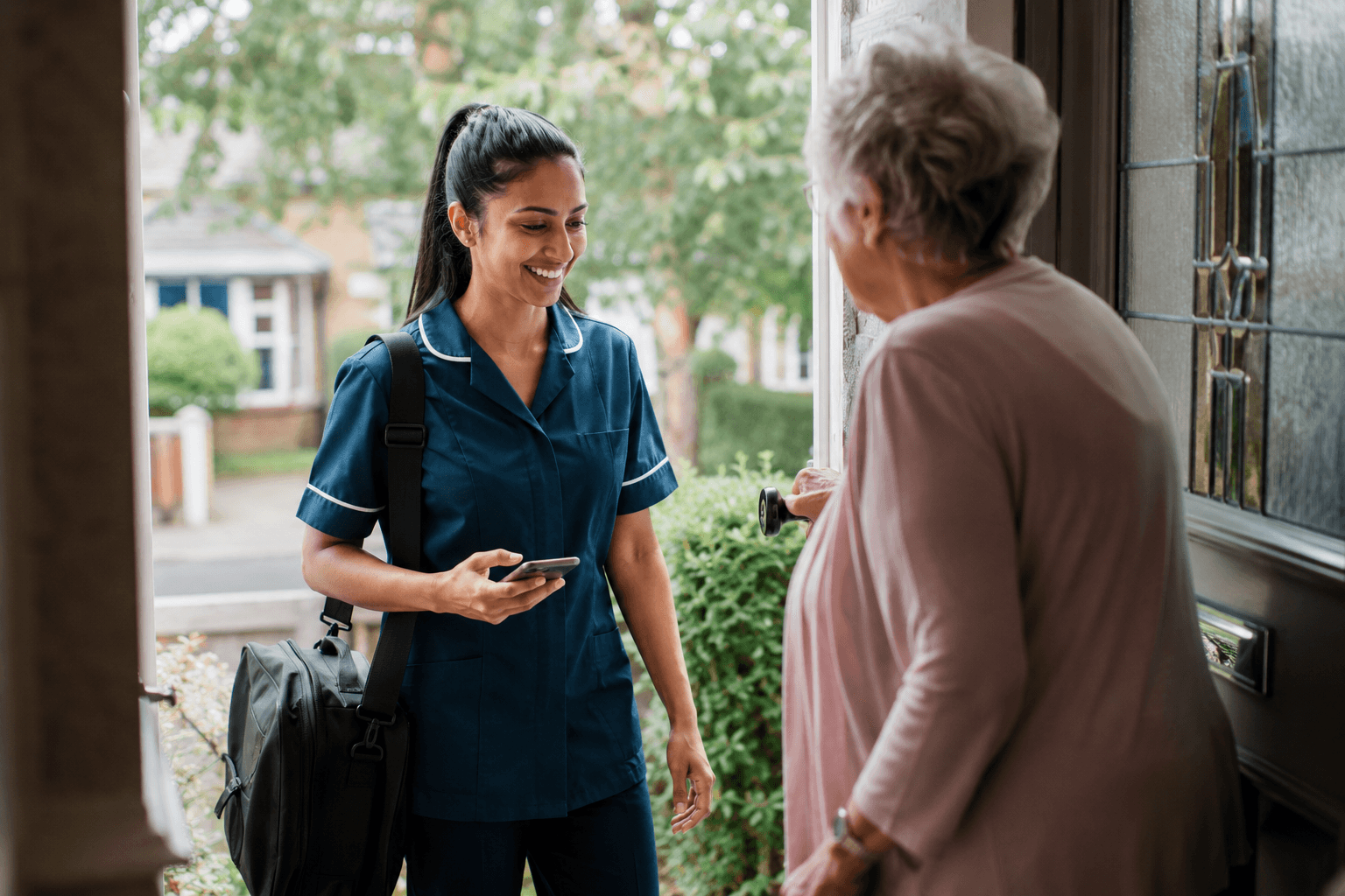 A visiting carer welcomed at a client's front door, phone in hand